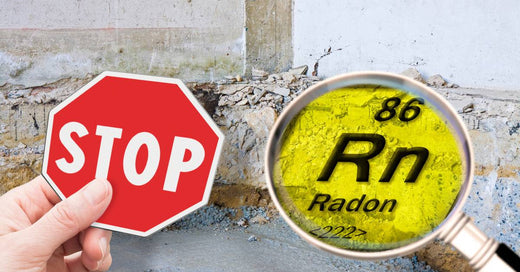 A hand holds a small red "STOP" sign next to a magnifying glass with the radon (Rn) symbol in front of a basement wall.