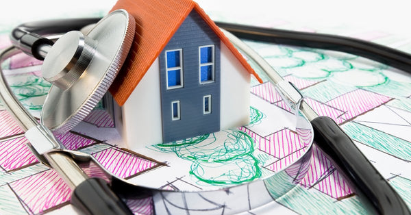 A stethoscope is wrapped around a small plastic model of a house that's sitting on top of hand-drawn building plans.