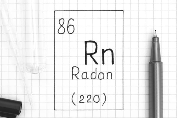 A test tube and a fine tipped marker lays on graph paper that reads "86 Rn Radon (220)" inside of a black square.