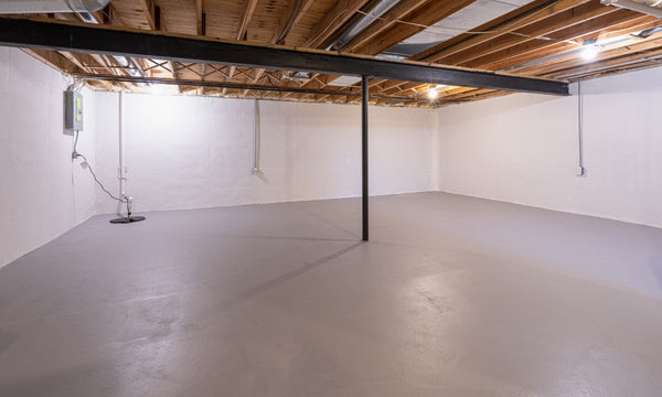 A grey concrete floor in a basement with exposed beams in the ceiling, showing its final appearance after an epoxy coating.